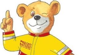 Ein Bär mit einer rot-gelben Rettungsjacke und einem Arztkoffer n der Hand